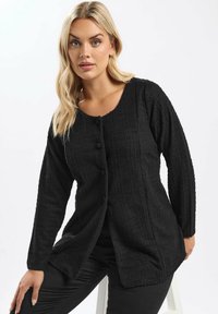 Cardigan nero in tessuto testurizzato con scollatura a girocollo, maniche lunghe e chiusura con bottoni frontali. Presenta un motivo a righe verticali e una vestibilità rilassata.