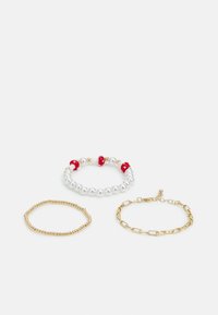 TrêsPulseiras: uma com pérolas brancas e contas vermelhas, uma fita fina de contas douradas, e uma pulseira de corrente dourada com fecho.