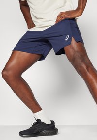 Navy athletic shorts with a streamlined design, featuring mesh accents and a logo badge. Lightweight fabric allows for ease of movement.