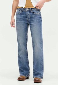 Ανοιχτό μπλε τζιν παντελόνι με ίσια γραμμή και ξεθωριασμένη υφή, που διαθέτει κλασικό σχέδιο πέντε τσεπών και μεταλλικό κούμπωμα, συνδυασμένο με καφέ μποτάκια.