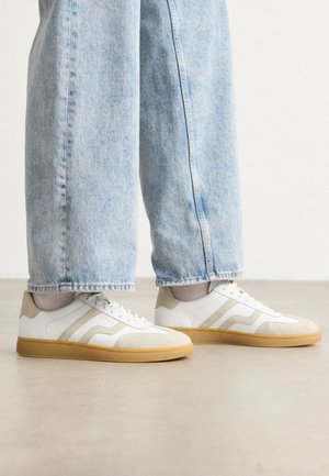 Zapatillas blancas con detalles en ante beige y suelas de goma clara; presentan un diseño de corte bajo y un acabado texturizado en la parte superior.