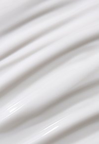 Crème blanche lisse et brillante étalée uniformément avec des crêtes douces et fluides et des reflets subtils à la surface.