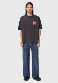 Szary bawełniany t-shirt z okrągłym logo w różowym nadruku na klatce piersiowej, w połączeniu z luźnymi niebieskimi dżinsami i czarnymi butami.