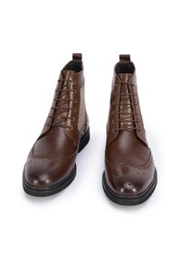 Botas de tobillo de cuero marrón con detalles de brogue, punta redonda y diseño de cordones. Paneles laterales texturizados y suela de goma para mayor durabilidad.