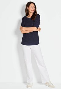 Marineblaues Strickoberteil mit kurzen Ärmeln, lockerer Passform und geripptem Saum, kombiniert mit weißen weit geschnittenen Hosen und hellen Sneakers.