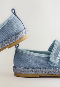 Niebieskie płótnowe buty z teksturowaną cholewką, plecionym niebieskim wykończeniem i lekką beżową podeszwą. Posiadają pętelkę z tyłu, co ułatwia zakładanie.