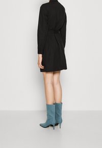 Vestito nero aderente con colletto e maniche lunghe, vita stretta e orlo svasato, abbinato a stivaletti alla caviglia azzurri chiari con punta affilata.