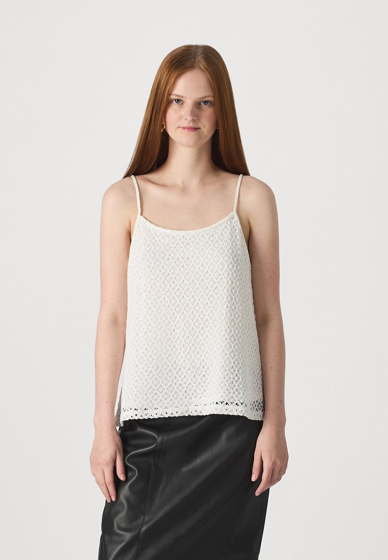 Hvit heklede tank-top med tynne stropper, med et åpent vevemønster og en bølget blonderkant, kombinert med et svart skinnskjørt.