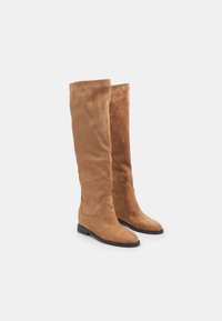 Botas marrones de ante por encima de la rodilla con suela plana negra, punta redonda y textura suave; diseño sin costuras sin sujetadores visibles.