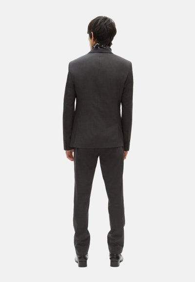 Grau maßgeschneiderter Anzug mit schlanker Passform; verfügt über einen einzelnen Schlitz auf der Rückseite und passende Hosen. Schwarze Schuhe runden das Outfit ab.