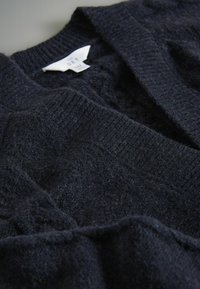 Tumši zils adīts kardigans ar ribotiem apkakli un fakturētu audumu. Ir etiķete ar uzrakstu "SET" gaišā krāsā.