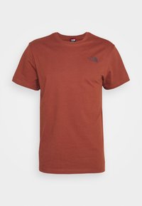 Camiseta de manga corta marrón de algodón con cuello redondo. Presenta un pequeño logo negro en la parte superior izquierda del pecho. Textura suave.