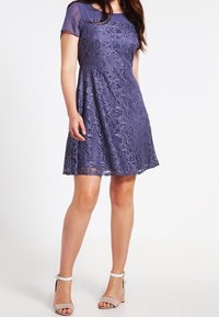 Robe en dentelle de couleur violet profond avec un corsage ajusté, des manches courtes en transparent et une jupe évasée. Texture douce avec des motifs floraux élaborés.