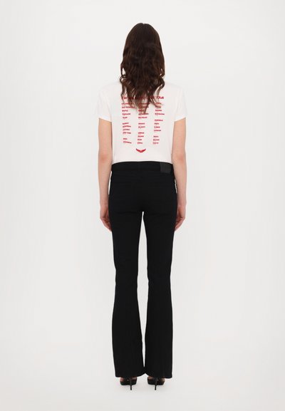 Maglietta bianca con grafica rossa sul retro, abbinata a pantaloni neri a campana. Il tessuto sembra liscio, con una silhouette aderente.