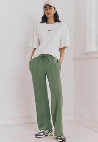 T-shirt bianco a vestibilità morbida con stampa "PARIS", abbinato a pantaloni della tuta larghi verde oliva con vita elastica e tasche laterali.