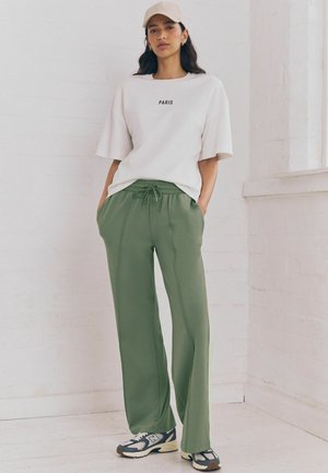 Tricou alb cu croială lejeră, cu imprimeu "PARIS", asortat cu pantaloni de trening lejeri de culoare verde măsliniu, cu talie elastică și buzunare laterale.