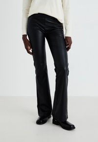 Black faux leather flared pants with a smooth texture, equipped with a high waist and tailored fit, paired with black ankle boots.