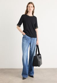 Haut noir à manches courtes avec des poignets à motifs, associé à un jean large bleu clair et un sac à main noir. Design épuré et simple.
