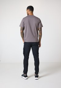 Grau Baumwoll-T-Shirt mit kurzen Ärmeln, kombiniert mit schwarzen Cargo-Hosen mit Seitentaschen. Sneaker mit weißen Sohlen und dunklen Akzenten.