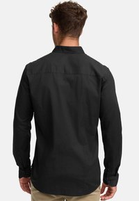 Camisa negra de manga larga con cuello, puños abotonados y una textura suave. Cuenta con un diseño recto en la espalda y un ajuste entallado.