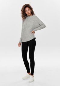 Pull gris ample avec des manches longues et un ourlet arrondi, associé à des leggings noirs et des baskets de couleur claire. Texture de tissu lisse.