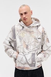 Sweatshirt com capuz apresentando um padrão de camuflagem com ramos e folhas, em tons de creme, cinza e castanho; punhos e cintura em malha canelada.