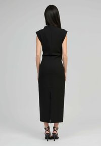 Robe midi noire avec des manches courtes, corsage ajusté et fente au dos. Fabriquée en tissu doux, elle présente un design épuré et minimaliste. Talons visibles.