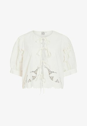 Hvit kort bluse med korte puff-ermene, blomsterformede hulldesign, bølget kant og knyting foran.