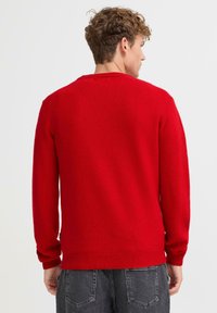 Czerwony sweter dziany z długimi rękawami, ściągaczami na mankietach i dole oraz okrągłym dekoltem. Miękka faktura, jednolity kolor bez widocznych wzorów.