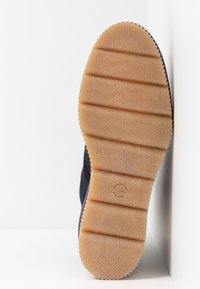 Suela de goma de un zapato con surcos horizontales, color marrón claro y superficie texturizada. Parte superior en color marino visible en el borde lateral.
