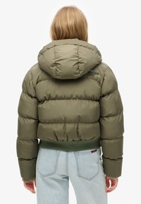 Olivgrön puffjacka med huva, ribbad ärmslut och nederkant, med fyllning och logotypdetalj på övre ryggen.
