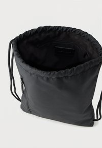 Μαύρη τσάντα με κορδόνι από λείο νάιλον με σφικτό επάνω μέρος, που διαθέτει εσωτερική τσέπη με φερμουάρ και απλό, μοντέρνο σχεδιασμό.