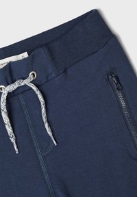 Navy zili treniņbikses ar regulējamu jostasvietu, ar metāla rāvējslēdzēja kabatu un strukturētu audumu. Ietver šuvju detaļas un mīkstu apdari.