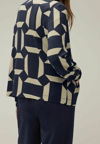 Pulovr v námořnické modři a krémové barvě se vzorem geometrických tvarů, žebrovanou texturou, dlouhými rukávy a volným střihem.