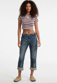 Crop top in paarse en witte strepen, high-waisted blauwe denim cargobroek met omgeslagen zomen, voorzien van zijzakken en een ontspannen pasvorm.