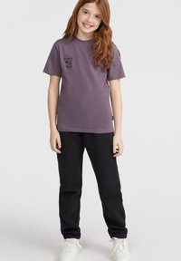 Szaro-fioletowy t-shirt z nadrukiem "Kobiety Fali", w połączeniu z czarnymi dresami z elastycznymi mankietami i białymi sneakersami.
