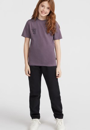 Grålig-lilla t-shirt med "Women of the Wave" print, parret med sorte joggere med elastiske manchetter og hvide sneakers.