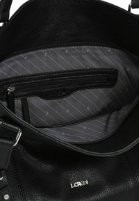 Schwarze Lederhandtasche mit einem Innenfutter aus grauem Material mit dezentem Streifenmuster. Enthält ein Reißverschlussfach und ein Logo-Detail.