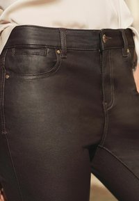 Jeans din denim negru cu un finisaj lucios. Prezintă un design standard cu cinci buzunare, accesorii metalice și detalii de cusătură în contrast.