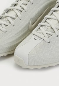 Gaiši pelēki sporta apavi ar teksturētu sieta augšdaļu, gludām akcentiem, izteiktu Nike logo un mīkstu zoli.