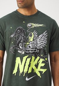 Camiseta de color verde oscuro con un diseño gráfico de un jinete con alas, marca Nike en un brillante verde lima y contornos negros llamativos.