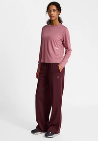 Top met lange mouwen en ronde hals in mauve stof, gecombineerd met wijde, bordeauxrode broek. Beide hebben een minimalistisch logo en een ontspannen pasvorm.