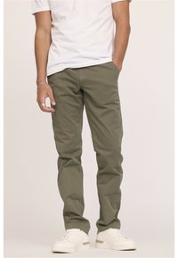 Pantalons verts olive en toile de coton, avec une coupe droite et des poches latérales. Associés à des baskets blanches.