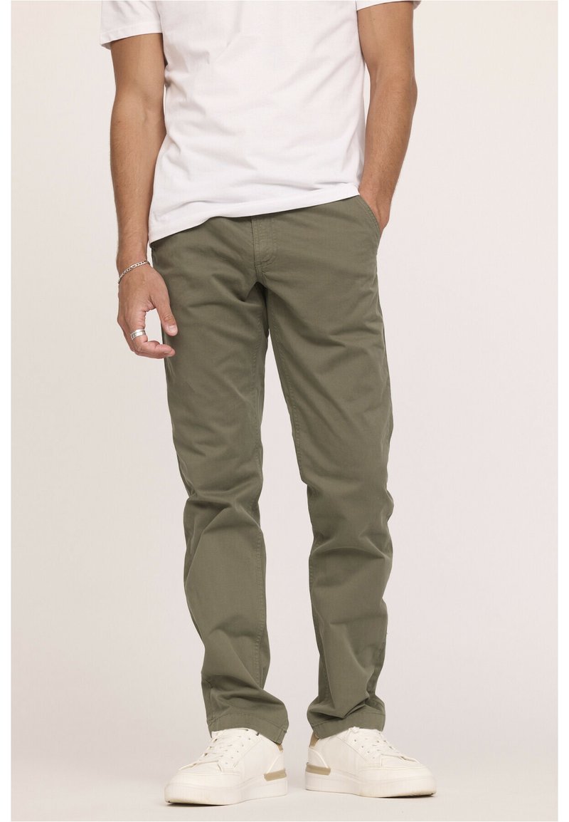 Pantalons verts olive en toile de coton, avec une coupe droite et des poches latérales. Associés à des baskets blanches.