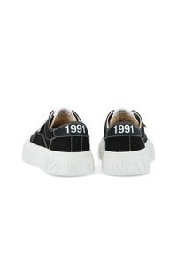 Baskets en toile noires avec une semelle en caoutchouc blanche. Présentent le numéro "1991" à l'arrière et des détails de couture blancs. Design minimaliste.