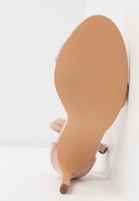 Růžový semišový podpatek se štíhlým stiletto. Podešev je světle hnědá s texturovaným gripem. Disponuje dvěma nastavitelnými pásky pro bezpečné uchycení.