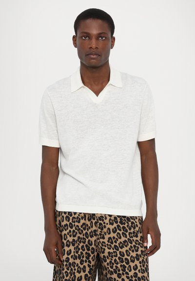 Short-sleeve, light gray polo shirt with a V-neck and contrasting white collar. Worn with brown shorts featuring a black leopard print pattern.