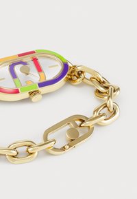 Montre dorée avec un boîtier ovale présentant un design à rayures multicolores. Bracelet en maillons avec fermeture à clip. Cadran argenté et index des heures.