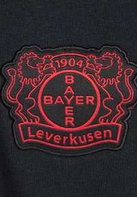 Tissu noir présentant un blason brodé avec deux lions, "Bayer" et "Leverkusen", ainsi que "1904" en détails rouges.