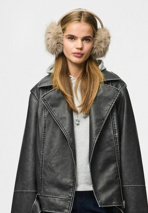 Zwarte faux leren jas met een opvallende kraag, gedragen over een grijze hoodie. Grote crèmekleurige faux bont oorkappen. Lang, steil haar.